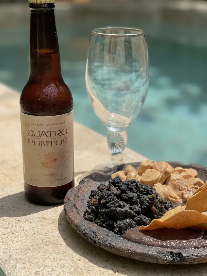 Botella Cuatro Puntos junto a una copa y botana frente a la alberca