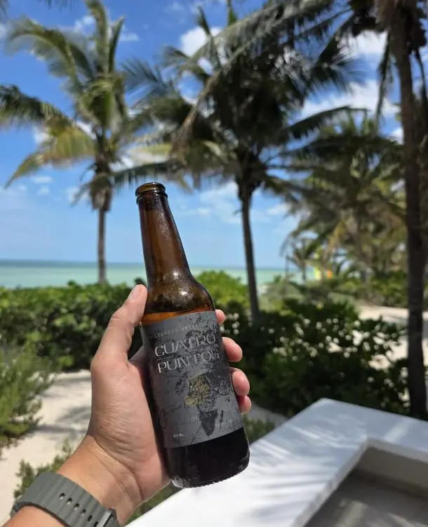 Botella Cuatro Puntos en mano frente a palmeras y mar